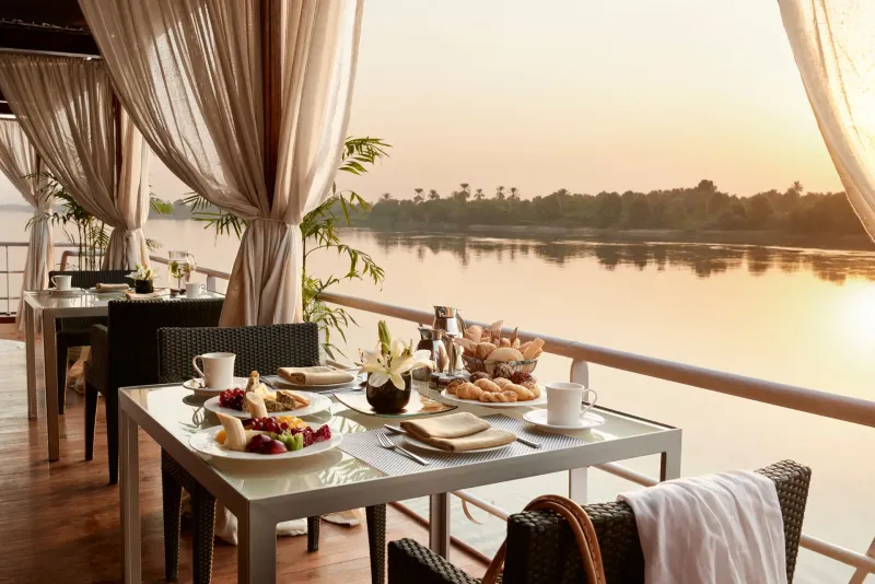 Sanctuary Nile Adventurer dining room with polished-wood floors and Nile views, or bar and lounge with oud trio evening entertainment, luxury Nile cruise Egypt 2026