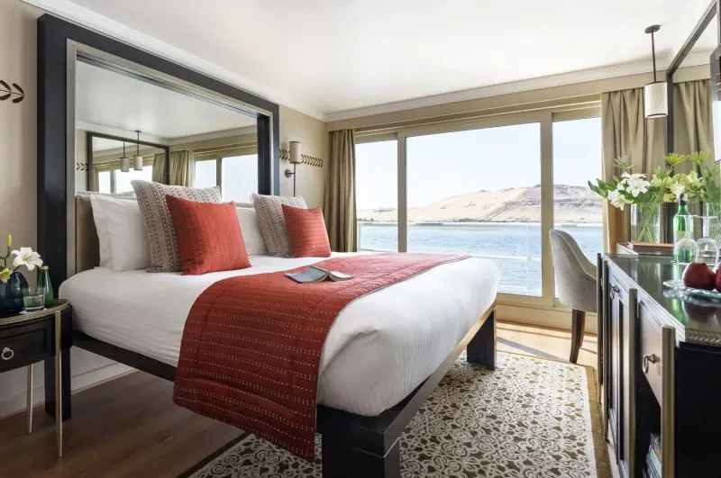 Sanctuary Sun Boat IV standard cabin — floor-to-ceiling windows with Nile views, four-poster bed with Egyptian linens, Art Deco design, luxury Nile cruise 2026