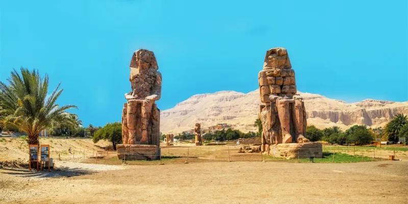 Colossi of Memnon at sunrise West Bank Luxor Egypt — statues facing east toward the Nile with Theban limestone cliffs 