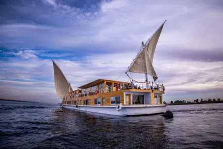 Nile cruise vs Dahabiya 2026 — traditional Dahabiya sailing boat on the Nile River Egypt at golden hour with lateen sails and desert cliffs